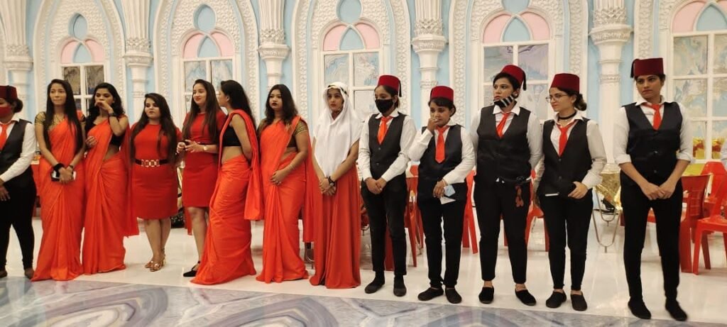 Food Forest Catering service team in orange sarees and black uniforms standing at decorated wedding venue