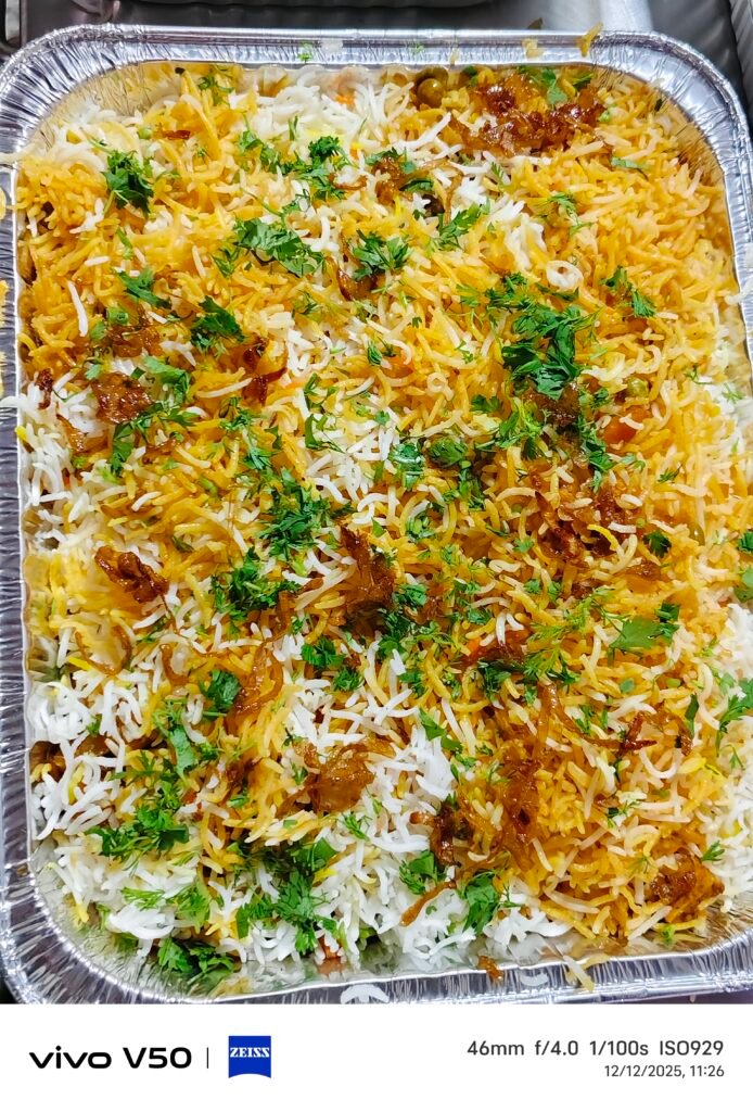 A top-down 9:16 vertical shot of a premium vegetable biryani presented in a rectangular foil tray on a dark wooden background. The dish features beautifully layered white and saffron-yellow basmati rice, generously topped with deeply caramelized fried onions and freshly chopped green cilantro leaves. Elegant gold text at the top reads "PREMIUM VEGETABLE BIRYANI".